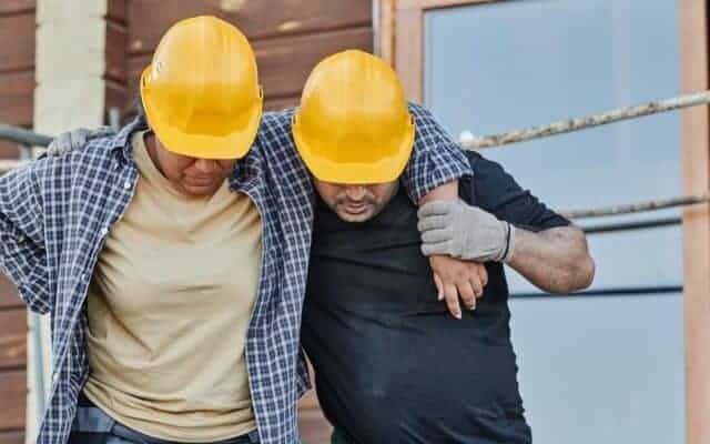Workers assisting each other on a construction site, emphasizing teamwork and safety.